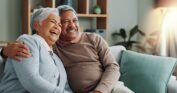 Happy, older couple embracing and laughing on a couch, illustrating the joyful well-being and consistent personal care provided by senior care for veterans.
