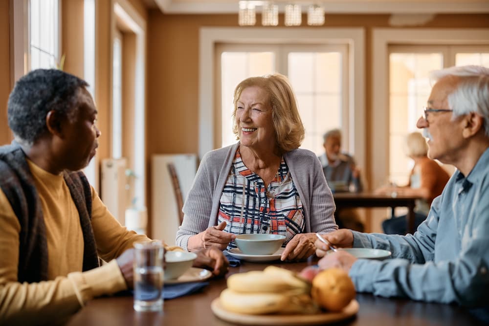 Happy residents dining together in a community setting, demonstrating the engaging lifestyle and pros of senior living communities.